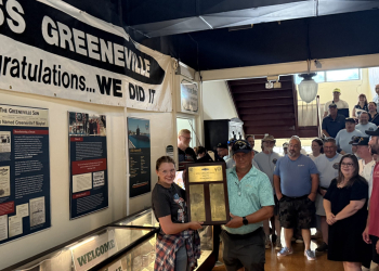 Flanked by former USS Greeneville sailors, Greeneville-Greene County Museum Director Sydney May, left, accepts a plaque for the museum from sailor Nickolas George. The plaque bears the name of every plank owner that sailed on the USS Greeneville.